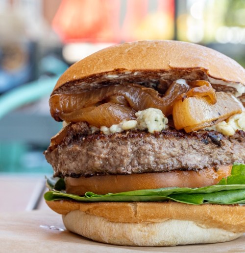Close-up of a juicy burger with grilled onions, lettuce, and tomato, served in a toasted bun.
