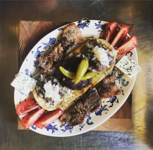 A platter of grilled meat, tortillas, onions, peppers, and fresh tomatoes on a decorative plate.