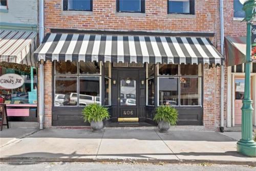 A storefront with a black and white striped awning, large windows, and potted plants on the sidewalk.