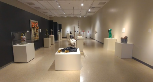 A spacious art gallery featuring various sculptures displayed on pedestals against neutral walls.