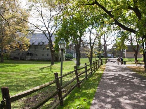 A scenic pathway lined with trees and a wooden fence, leading to a historic building in a lush green park.