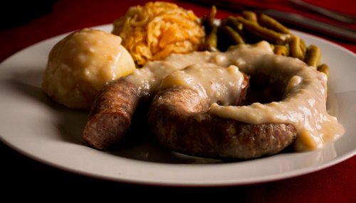 A plate featuring sausage with gravy, mashed potatoes, green beans, and a side of noodles.