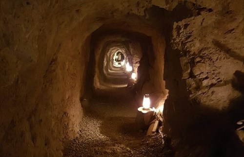 A dimly lit tunnel with rocky walls and lanterns lining the path, creating a mysterious atmosphere.