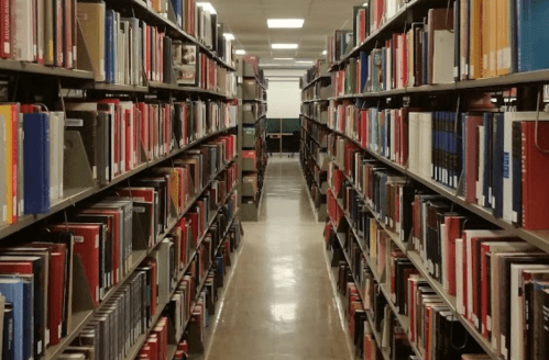 A view of a library aisle lined with shelves filled with colorful books on both sides.
