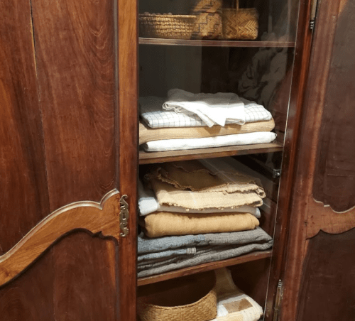 A wooden cabinet with glass doors displaying neatly folded linens and woven baskets on shelves.