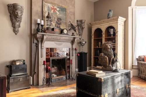 A cozy room featuring a decorative fireplace, bookshelves, and vintage furniture, with an owl statue and candles.