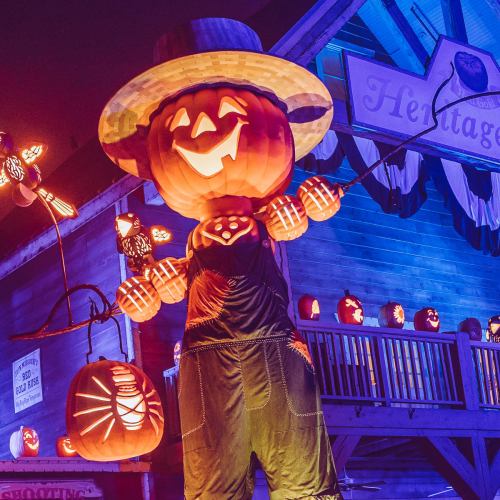 A festive Halloween scene featuring a scarecrow with a pumpkin head, surrounded by glowing jack-o'-lanterns.