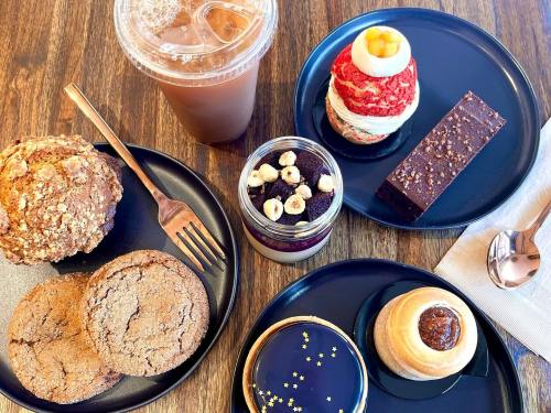 A variety of desserts on black plates, including cookies, a layered dessert, and a drink, on a wooden table.