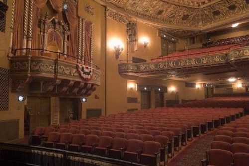 Interior of a vintage theater featuring ornate architecture and rows of red seats.