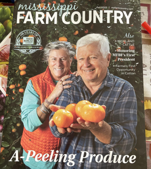 A couple smiles while holding oranges, surrounded by citrus trees, on the cover of Mississippi Farm Country magazine.