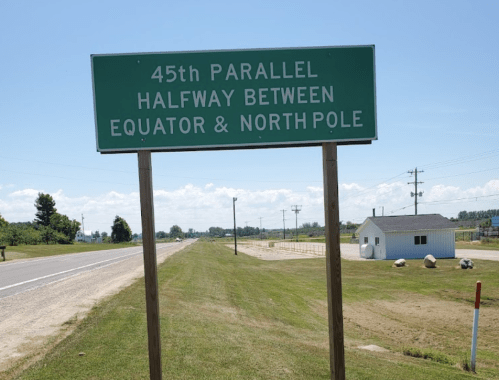 Sign indicating the 45th parallel, halfway between the Equator and North Pole, alongside a rural road.