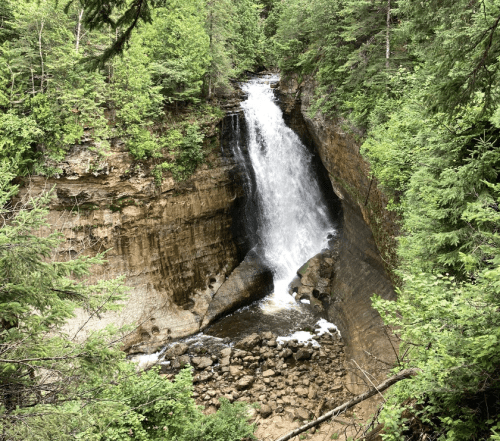 A waterfall cascades down rocky cliffs, surrounded by lush green trees and foliage.