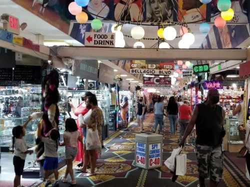 A bustling indoor market with colorful lights, shops, and people browsing, including families and individuals.