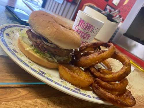 A plate with a fried chicken sandwich topped with lettuce and a side of crispy onion rings.