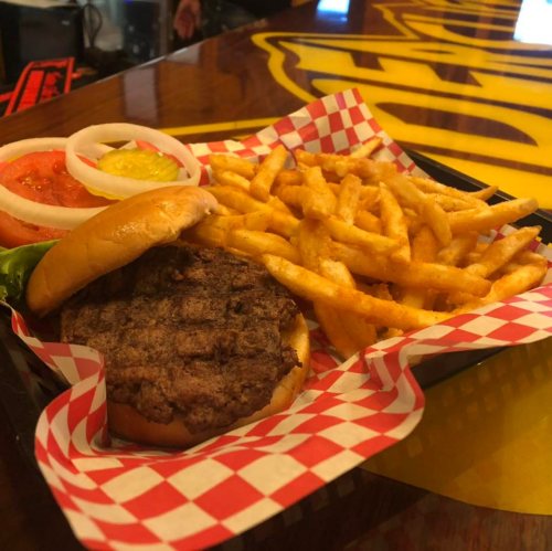 A juicy burger with lettuce, tomato, onion, and pickles, served with a side of crispy fries in a checkered basket.