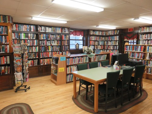 A cozy library with bookshelves filled with books, a table, and chairs for reading and studying.