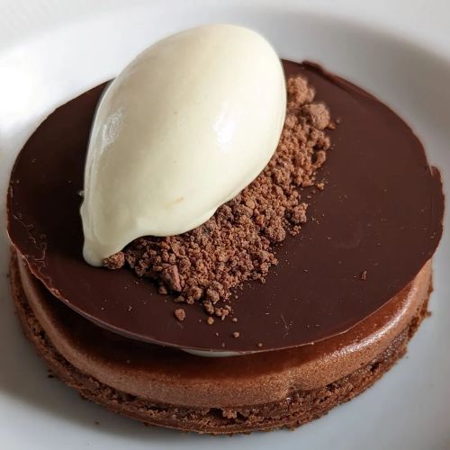 A decadent chocolate dessert topped with a scoop of cream and chocolate crumbs on a round base.