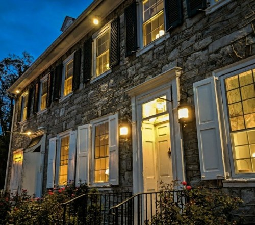 A historic stone building at dusk, illuminated by warm lights, with windows and a welcoming front door.