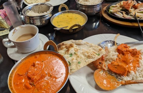 A table spread with Indian dishes, including curry, rice, naan, and a cup of tea.