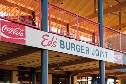Sign for "Ed's Burger Joint" with Coca-Cola branding, featuring a vibrant outdoor seating area.