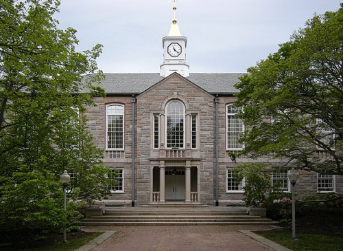 A stone building with a clock tower, surrounded by trees and a pathway leading to the entrance.