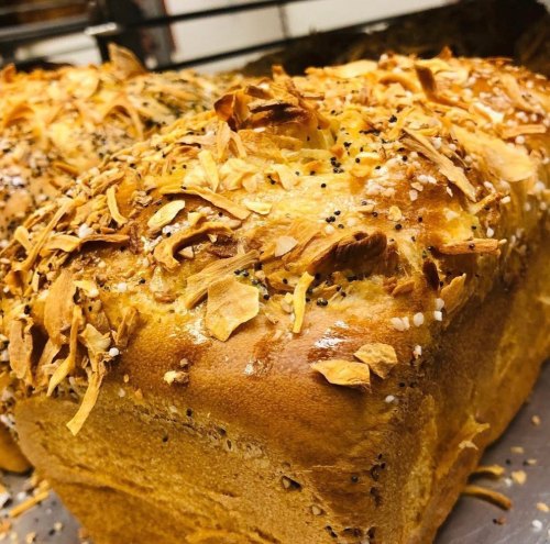 Freshly baked bread loaf topped with crispy flakes and seeds, golden brown and inviting.