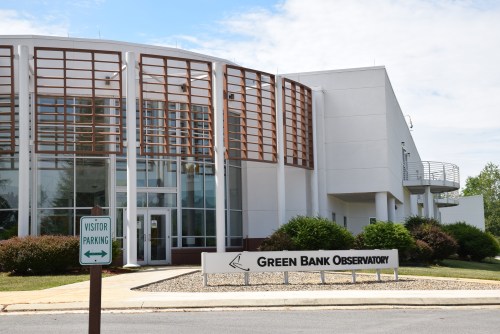 Exterior view of the Green Bank Observatory building with a visitor parking sign in front.