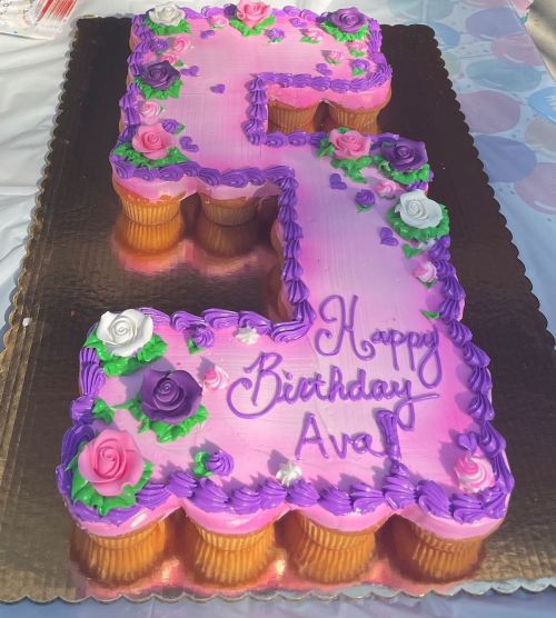 A large birthday cake shaped like the number 5, decorated with pink frosting, flowers, and "Happy Birthday Ava!" written on it.