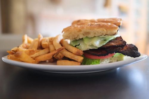 A plate with a sandwich stacked with lettuce, tomato, and grilled meat, accompanied by a side of golden fries.