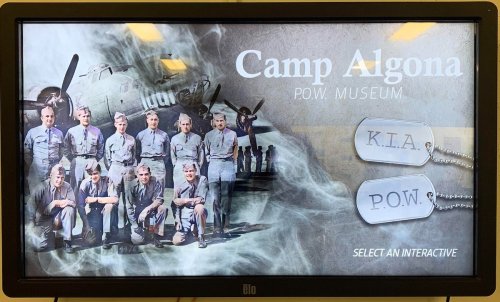 Display screen for Camp Algona P.O.W. Museum featuring a historical photo of soldiers and dog tags labeled K.I.A. and P.O.W.