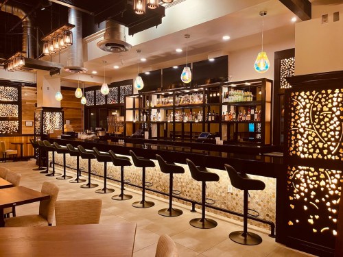 A modern bar with illuminated shelves, stylish seating, and decorative partitions in a warm, inviting atmosphere.