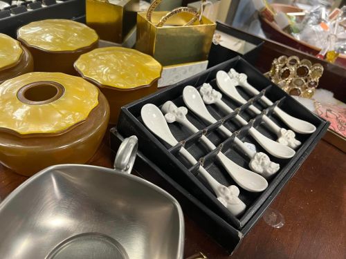 A collection of decorative items, including small spoons, containers, and jewelry, arranged on a wooden surface.