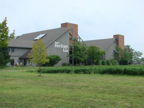 A large, two-story building with a sign reading "Heritage Inn," surrounded by greenery and open fields.