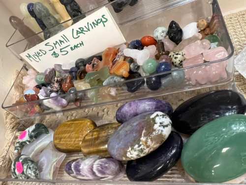 A display of various small carved gemstones in clear containers, labeled "Mixed Small Carvings $5 each."