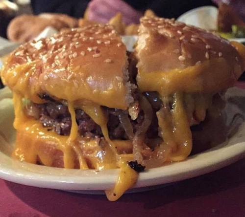 A close-up of a cheeseburger with melted cheese, sesame seed bun, and a juicy beef patty, partially cut in half.