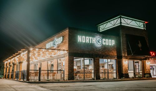 A well-lit restaurant building at night, featuring the sign "NORTH COOP" and outdoor seating.