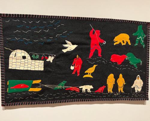 A colorful textile artwork depicting Arctic scenes with figures, animals, and an igloo against a dark background.
