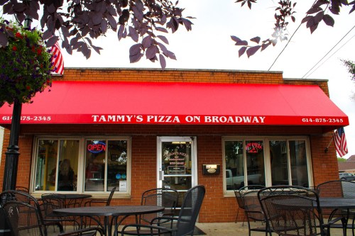 Exterior of Tammy's Pizza on Broadway, featuring a red awning, open sign, and outdoor seating.
