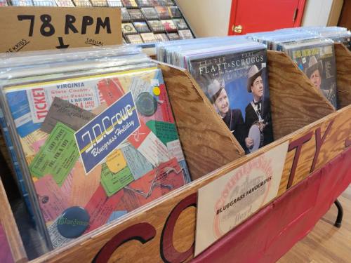 A wooden display holds vintage vinyl records, featuring colorful album covers and a sign reading "Bluegrass Favorites."