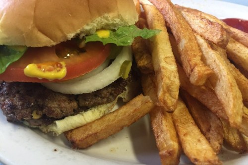 A juicy hamburger with lettuce, tomato, onion, and condiments, served with a side of golden French fries.