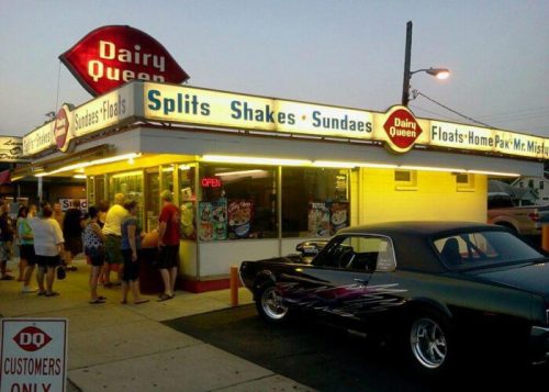 A Dairy Queen with a crowd outside, featuring a vintage car parked nearby and a bright, inviting sign.