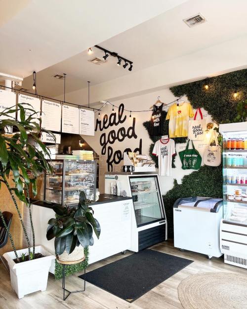 A cozy café interior featuring a counter, menu board, merchandise, and plants, with a welcoming atmosphere.