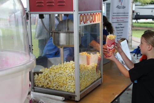 A popcorn machine overflowing with fresh popcorn, while a child holds a striped container ready to be filled.