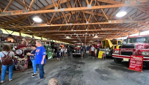 A crowded indoor venue showcasing vintage trucks, with people exploring and admiring the vehicles on display.