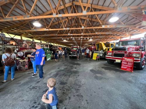 A spacious indoor venue filled with vintage trucks, people exploring, and informational signs about the vehicles.