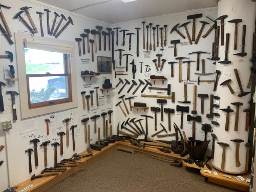 A wall display filled with various hand tools, including hammers and axes, in a well-lit room.