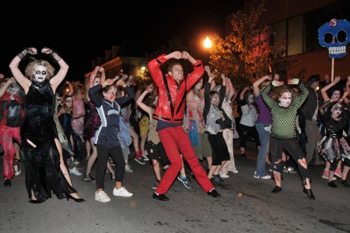 A group of people in Halloween costumes dancing in the street at night, with spooky decorations and festive energy.
