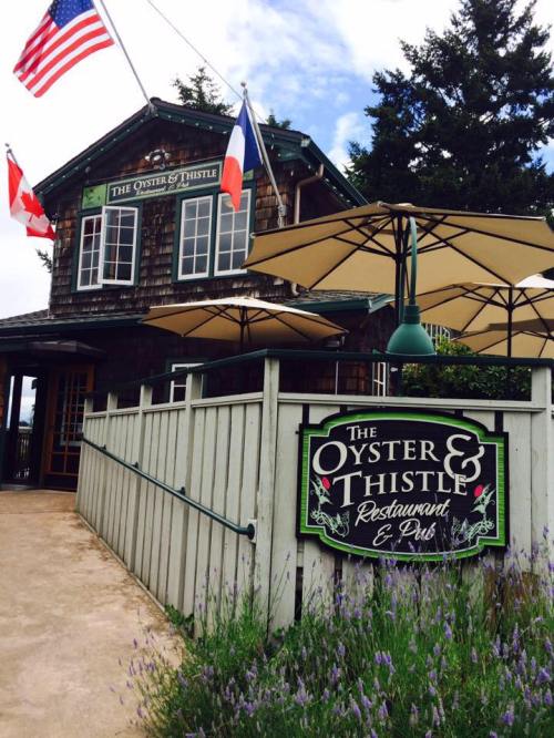 Exterior of The Oyster & Thistle Restaurant & Pub, featuring flags and outdoor seating under umbrellas.