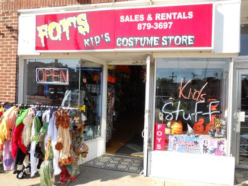 A colorful storefront of a kids' costume store with costumes displayed outside and an "Open" sign in the window.