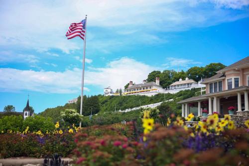 A vibrant landscape featuring a flagpole with the American flag, colorful flowers, and a hillside hotel under a blue sky.